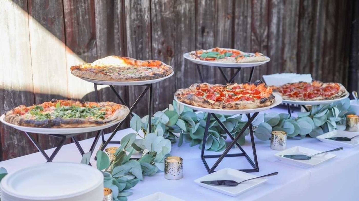 A spread of Woodfire Pies pizzas staged on risers at a catered event